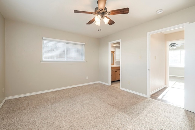 unfurnished bedroom featuring ensuite bath, multiple windows, baseboards, and light colored carpet