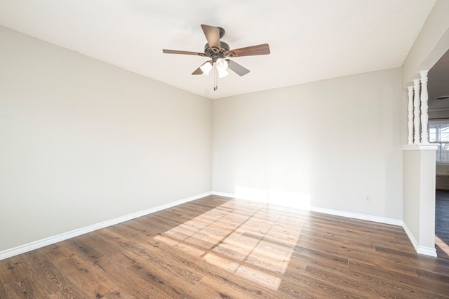 empty room featuring a ceiling fan, ornate columns, baseboards, and wood finished floors