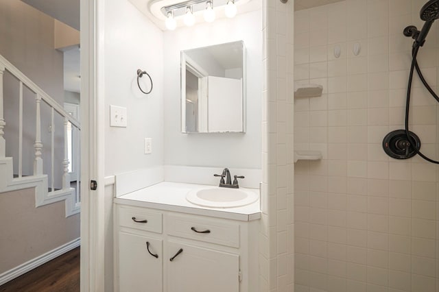 bathroom featuring tiled shower, vanity, baseboards, and wood finished floors