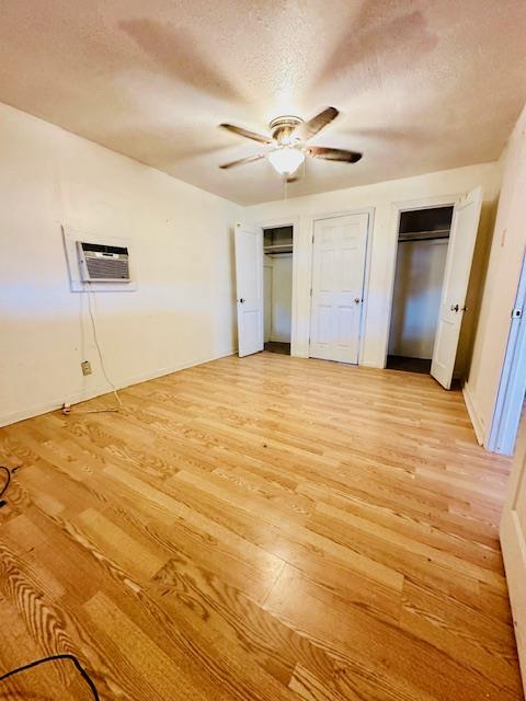 unfurnished bedroom featuring two closets, ceiling fan, a textured ceiling, light hardwood / wood-style floors, and a wall unit AC