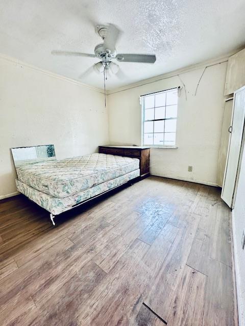 unfurnished bedroom featuring ceiling fan, crown molding, a textured ceiling, and hardwood / wood-style flooring