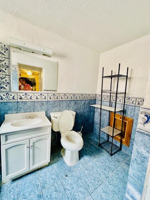 bathroom with vanity, tile patterned flooring, toilet, a textured ceiling, and tile walls