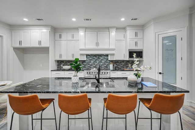 kitchen featuring a breakfast bar area, a large island with sink, sink, and white cabinets