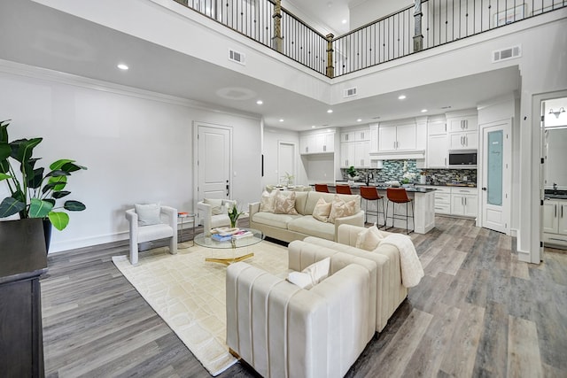 living room with crown molding, a towering ceiling, and light wood-type flooring