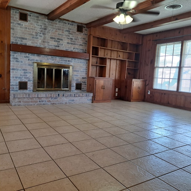 unfurnished living room with wooden walls, ceiling fan, a fireplace, a textured ceiling, and beam ceiling