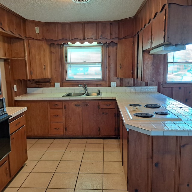 kitchen with tile counters, sink, white electric cooktop, oven, and light tile patterned floors