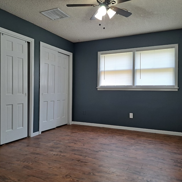 unfurnished bedroom featuring a textured ceiling, ceiling fan, dark wood-type flooring, and multiple closets