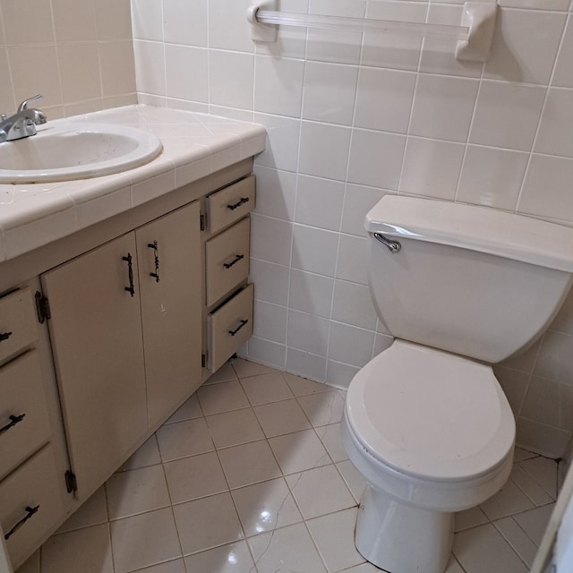 bathroom with toilet, vanity, tile patterned floors, and tile walls