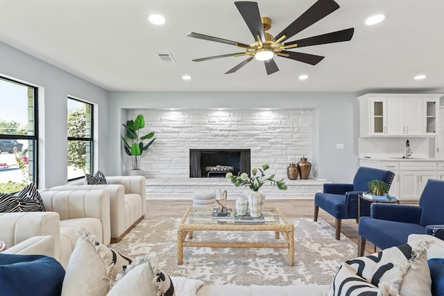 living room with ceiling fan, a fireplace, light hardwood / wood-style floors, and sink