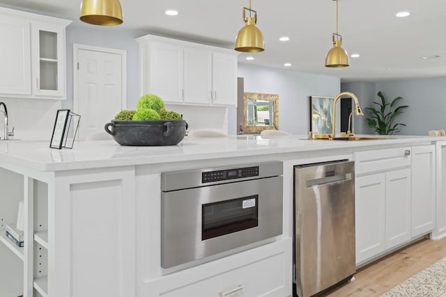 kitchen with light stone countertops, pendant lighting, light hardwood / wood-style flooring, white cabinets, and oven