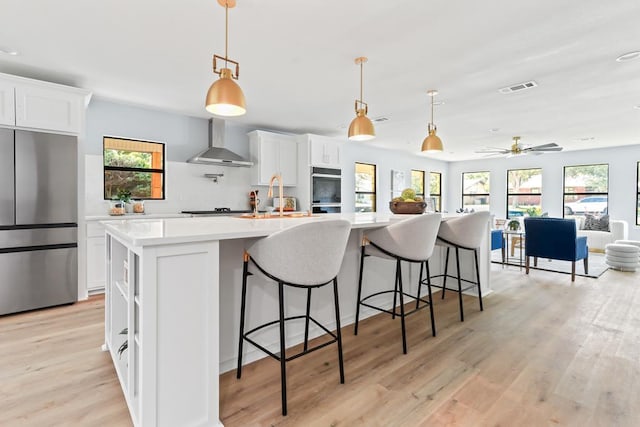 kitchen with wall chimney exhaust hood, stainless steel fridge, and a healthy amount of sunlight