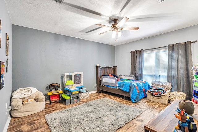 bedroom with ceiling fan, a textured ceiling, baseboards, and wood finished floors