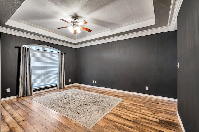 spare room featuring ornamental molding, wood finished floors, a textured ceiling, and a raised ceiling