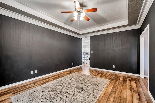 empty room featuring baseboards, a raised ceiling, ceiling fan, wood finished floors, and crown molding