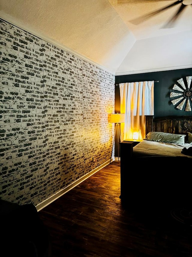 bedroom with vaulted ceiling, brick wall, dark wood-type flooring, and a textured ceiling