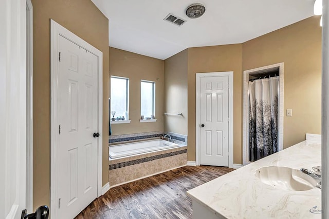 bathroom featuring double vanity, visible vents, wood finished floors, a garden tub, and a sink