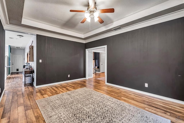 spare room featuring visible vents, a raised ceiling, wood finished floors, and ornamental molding