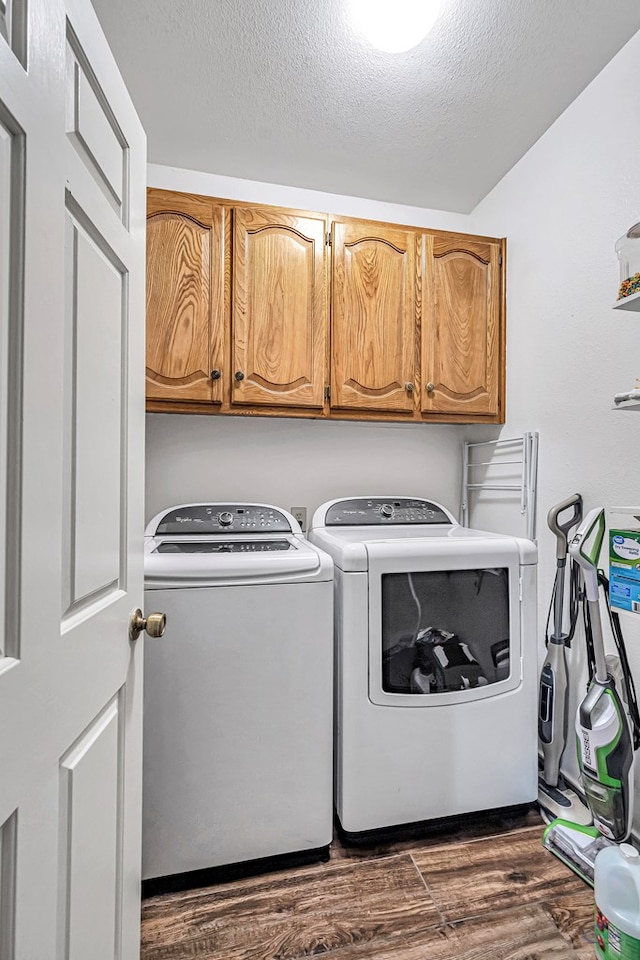 clothes washing area featuring cabinet space, washing machine and dryer, a textured ceiling, and dark wood-type flooring