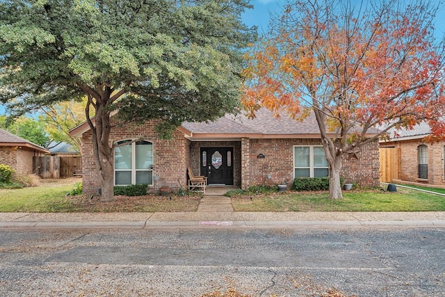 ranch-style home with a shingled roof, fence, a front lawn, and brick siding