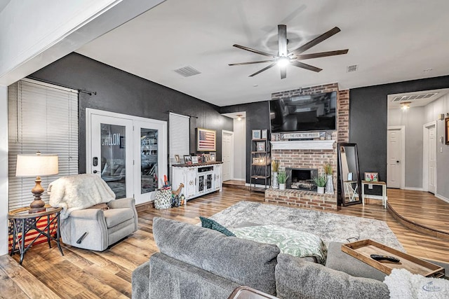 living room with a ceiling fan, a fireplace, visible vents, and wood finished floors