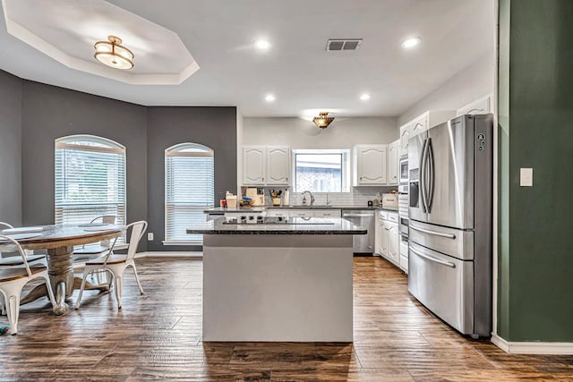 kitchen featuring visible vents, a kitchen island, appliances with stainless steel finishes, white cabinetry, and a sink