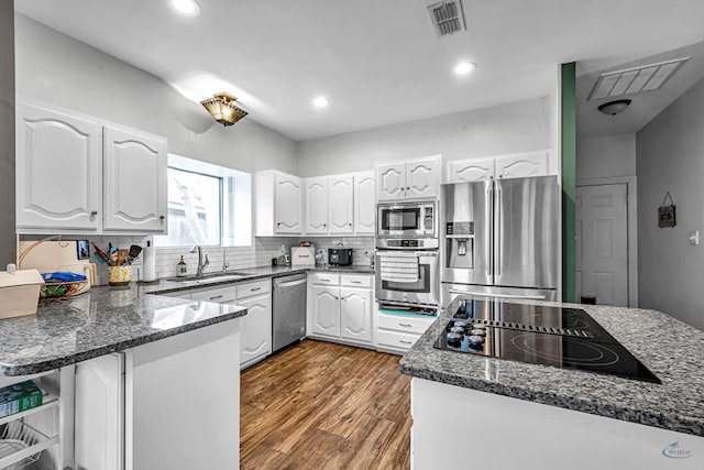 kitchen with visible vents, appliances with stainless steel finishes, white cabinets, a sink, and dark stone counters