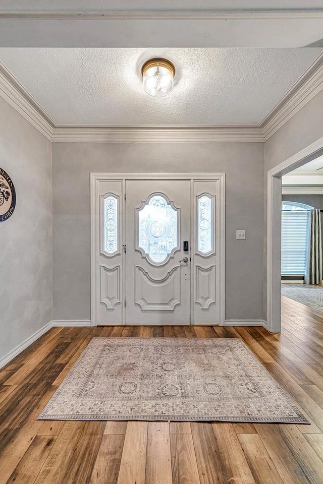 entrance foyer featuring ornamental molding, a textured ceiling, baseboards, and wood finished floors