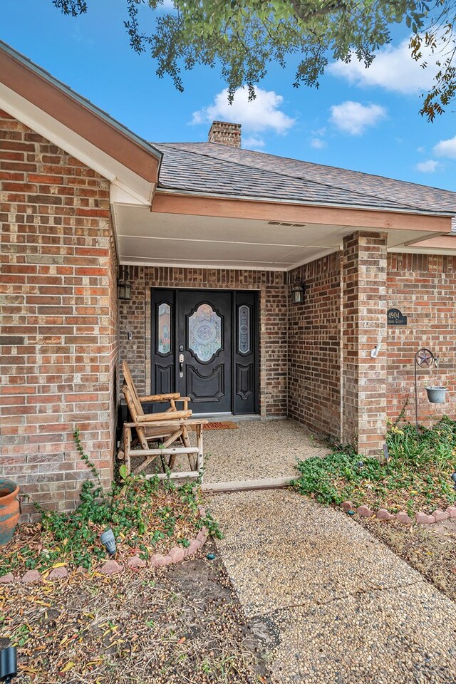 property entrance with roof with shingles, brick siding, and a chimney