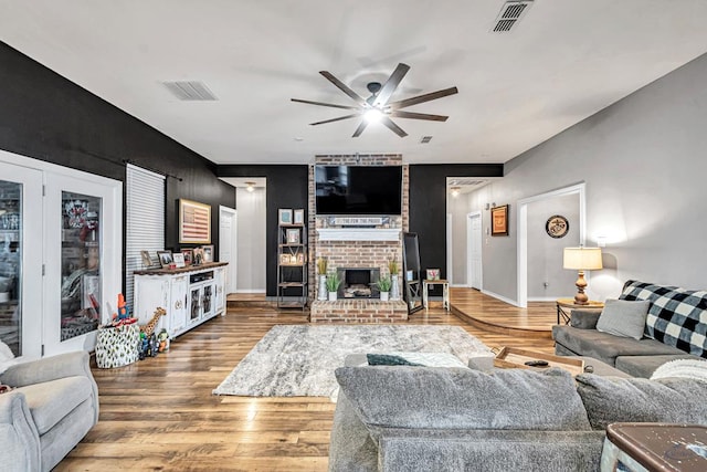 living room featuring ceiling fan, a brick fireplace, wood finished floors, and visible vents