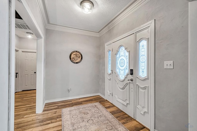 foyer with a textured ceiling, wood finished floors, visible vents, baseboards, and ornamental molding