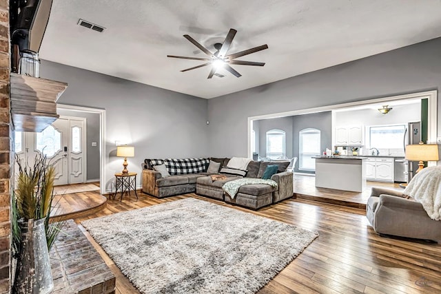 living area with a wealth of natural light, visible vents, ceiling fan, and wood finished floors