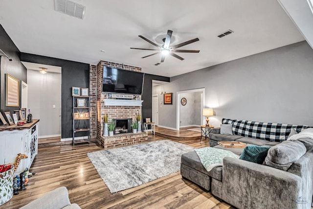 living area featuring ceiling fan, a fireplace, visible vents, and wood finished floors