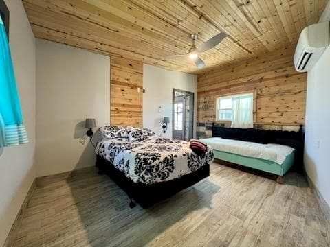 bedroom with a wall mounted air conditioner, wood walls, and hardwood / wood-style floors