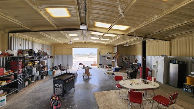 garage featuring white refrigerator with ice dispenser, a workshop area, and stainless steel refrigerator