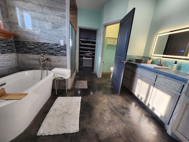 bathroom with vanity, a washtub, toilet, tile walls, and concrete flooring