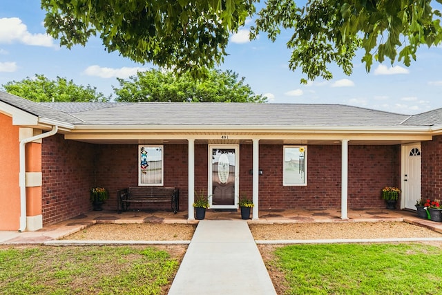 491 County Rd 202, Seminole, TX 79360 - property entrance with covered porch, brick siding, a shingled roof, and a yard