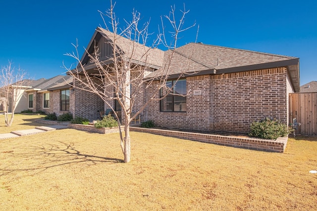 view of home's exterior with roof with shingles, fence, a lawn, and brick siding