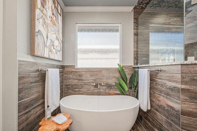 bathroom with ornamental molding, a freestanding tub, a wainscoted wall, and tile walls