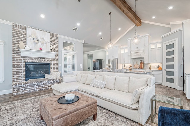 living area featuring beam ceiling, visible vents, ornamental molding, light wood-type flooring, and plenty of natural light