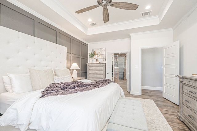 bedroom with a raised ceiling, visible vents, ornamental molding, ceiling fan, and wood finished floors