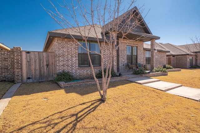 view of front of home with a gate, fence, a front lawn, and brick siding