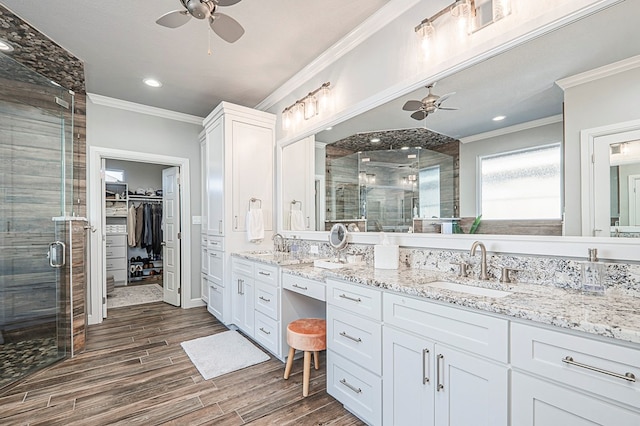 bathroom featuring wood finish floors, a sink, a ceiling fan, a walk in closet, and crown molding