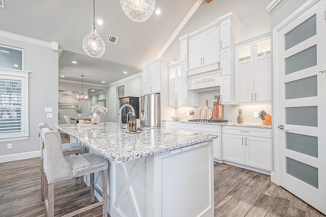 kitchen featuring pendant lighting, visible vents, appliances with stainless steel finishes, white cabinets, and an island with sink