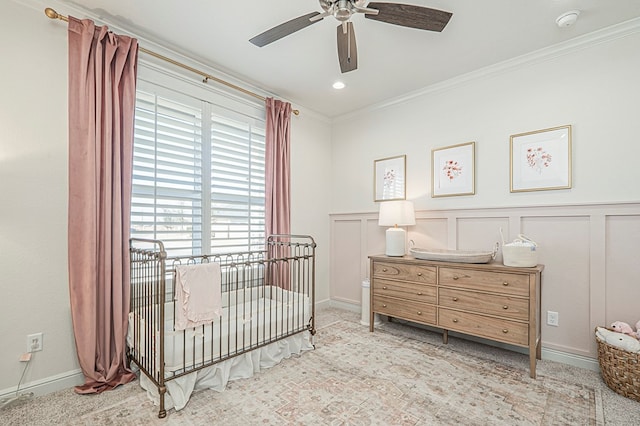 bedroom with baseboards, a ceiling fan, ornamental molding, a nursery area, and a decorative wall