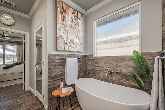 bathroom with visible vents, connected bathroom, wainscoting, crown molding, and a freestanding tub