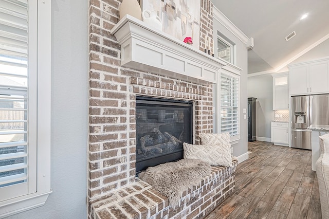 interior space with stainless steel fridge, visible vents, decorative backsplash, wood finished floors, and a fireplace