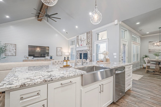 kitchen with an island with sink, white cabinets, a sink, and decorative light fixtures