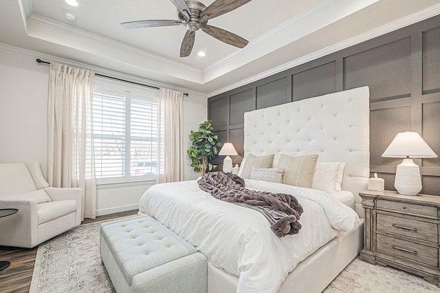 bedroom featuring crown molding, a tray ceiling, wood finished floors, and a decorative wall