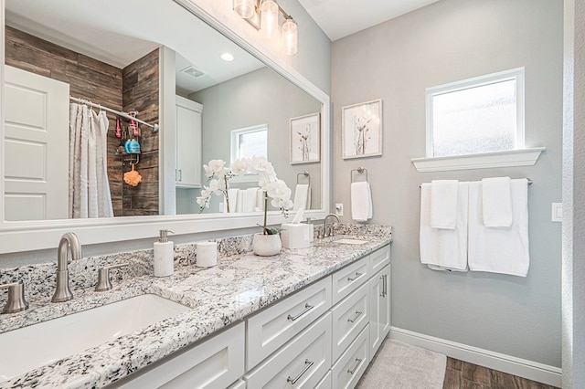 bathroom with double vanity, wood finished floors, a sink, and baseboards