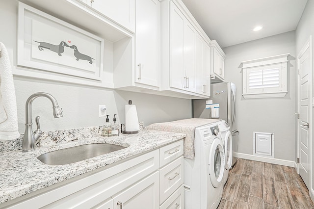 washroom featuring washing machine and dryer, a sink, baseboards, cabinet space, and light wood finished floors